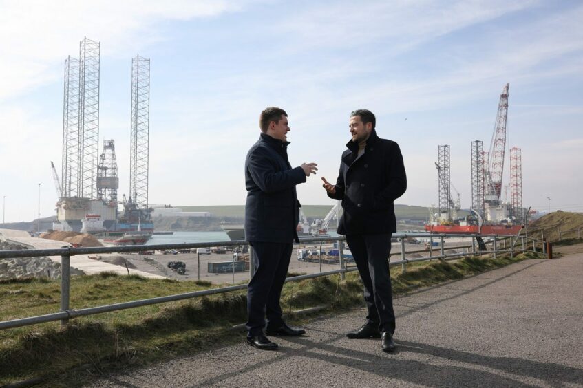 Martin Welsh and Kieran Taylor stood in front of oil rigs in Aberdeen.