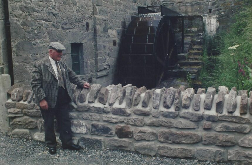 Johnny Turner standing next to the waterwheel of Benholm Mill.