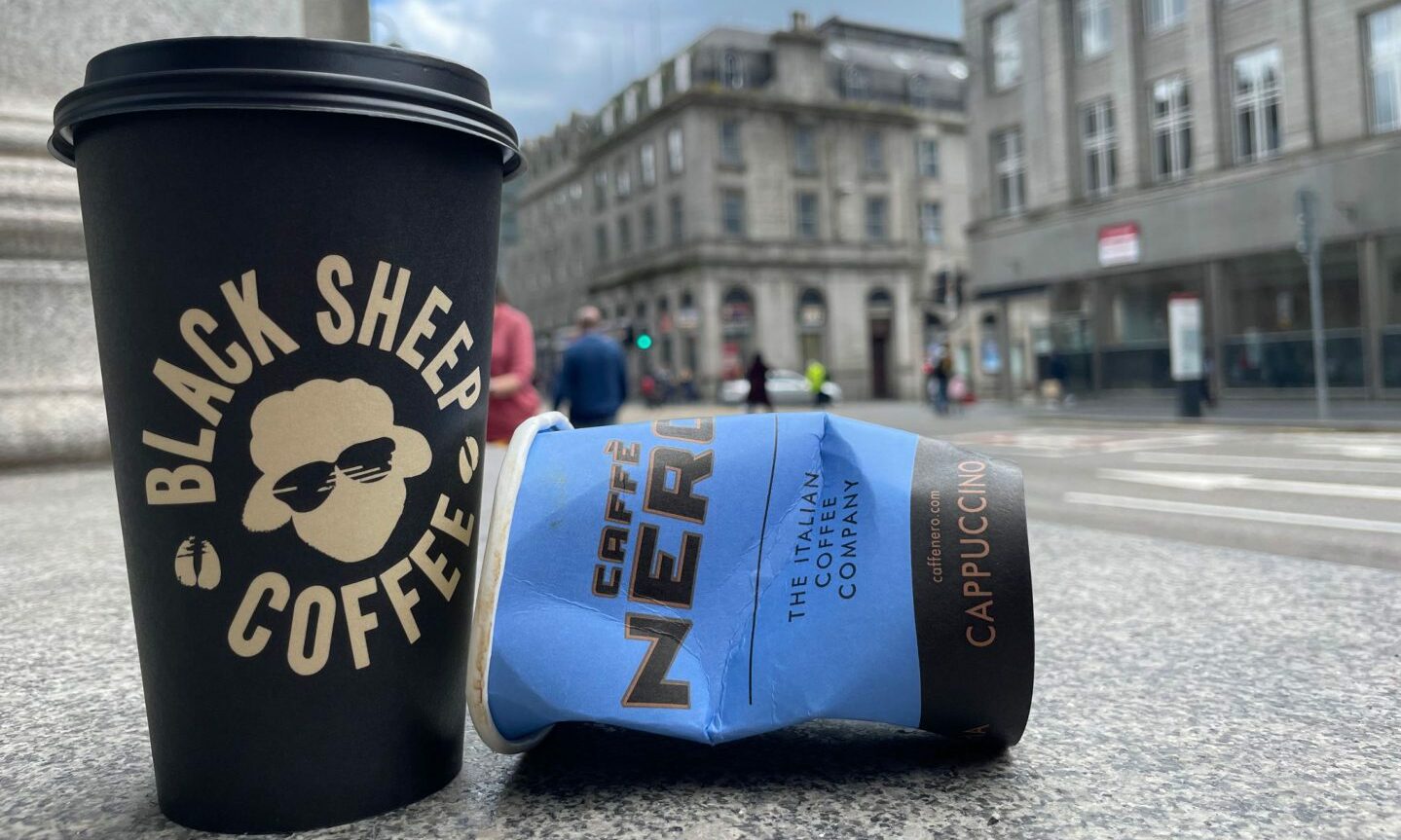 A black sheep coffee to-go cup next to a crumpled Caffe Nero to-go cup