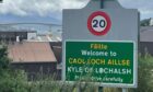 Close-up of 20mph sign at Kyle of Lochalsh with Skye bridge behind.
