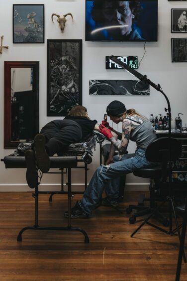 Tattoo artist doing tatto on client's arm.