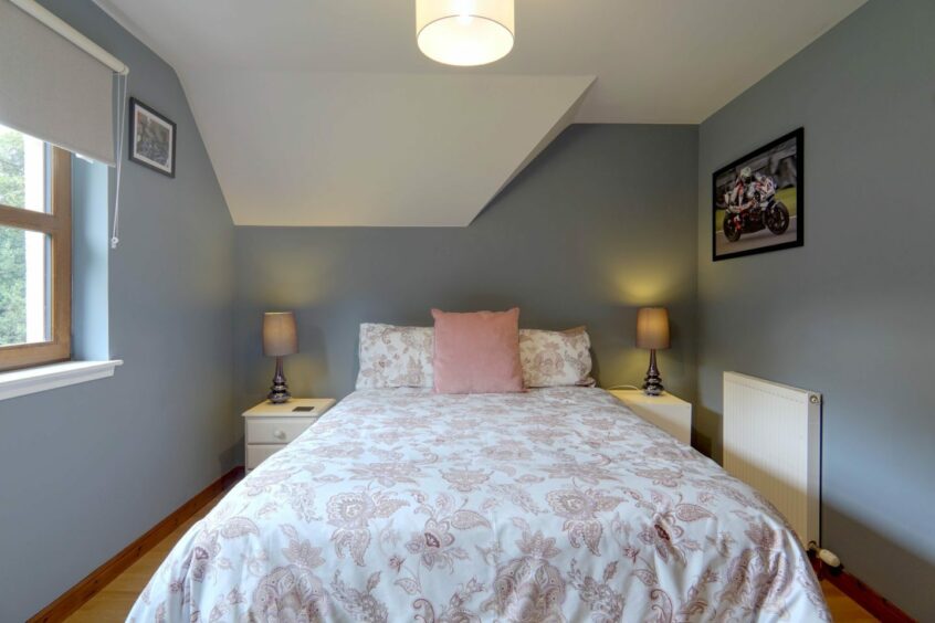 A bedroom in the Moray country cottage with blue walls, wooden floors and pink floral bedsheets