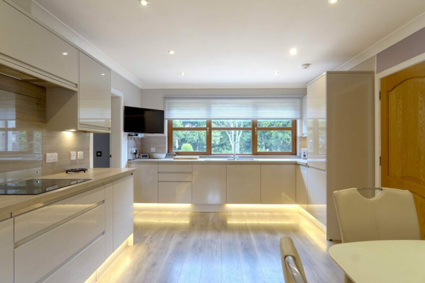 The kitchen in the cottage with sleek white counters and an inbuilt hob and fridge. There is a wall-mounted TV