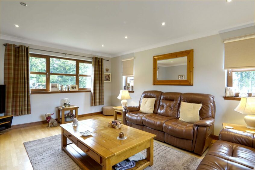 A living room in the Moray Country cottage featuring leather sofas, a wooden coffee table, a Television and two large windows