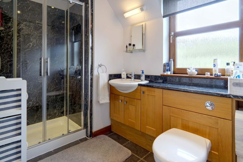 The en suite shower room, with a walk-in shower with glass doors, white walls, wooden cabinets with black counter tops and a frosted window.