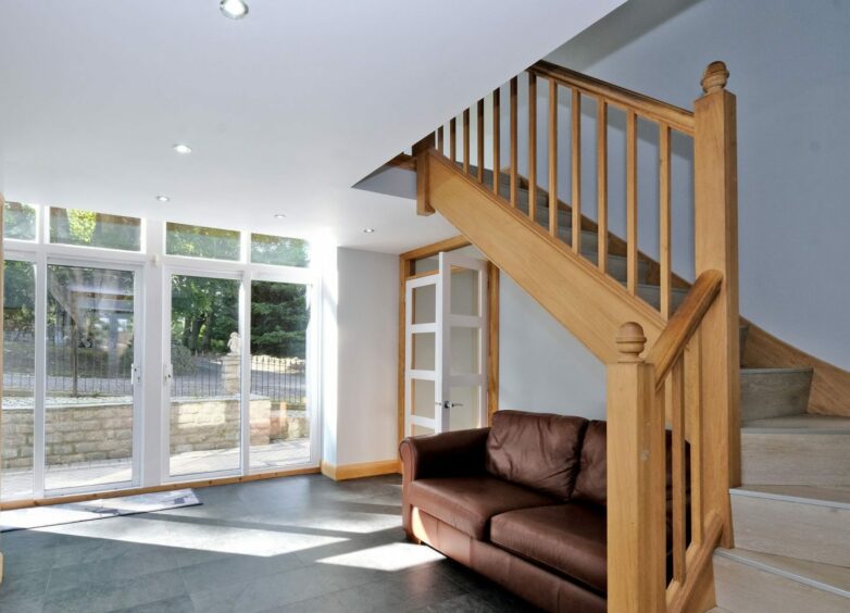A room with glass patio doors, a leather sofa and stairs leading to the first floor