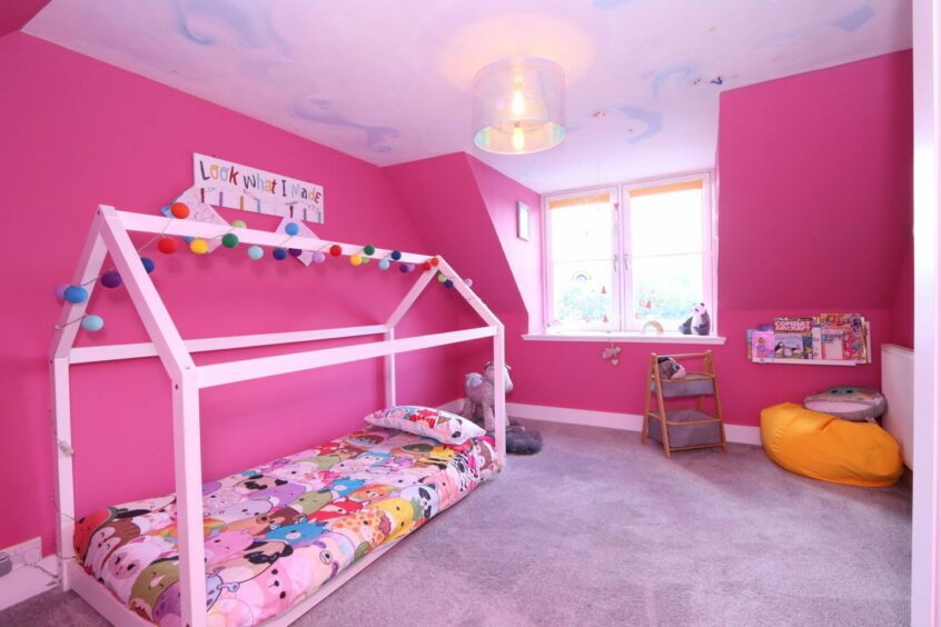 A bright pink children's bedroom in the royal deeside property, featuring pastel  pink, purple and blue painted ceiling, a pink framed bed with multi-coloured fairy lights and a large window.