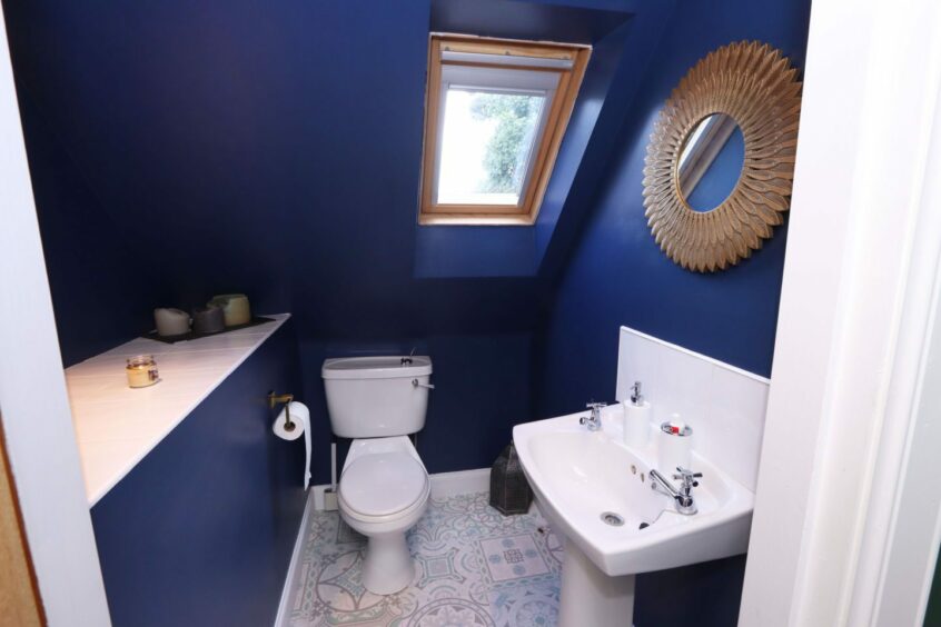 One of the bathrooms in the cottage has dark blue walls, a statement mirror and blue and white patterned floor tiles.