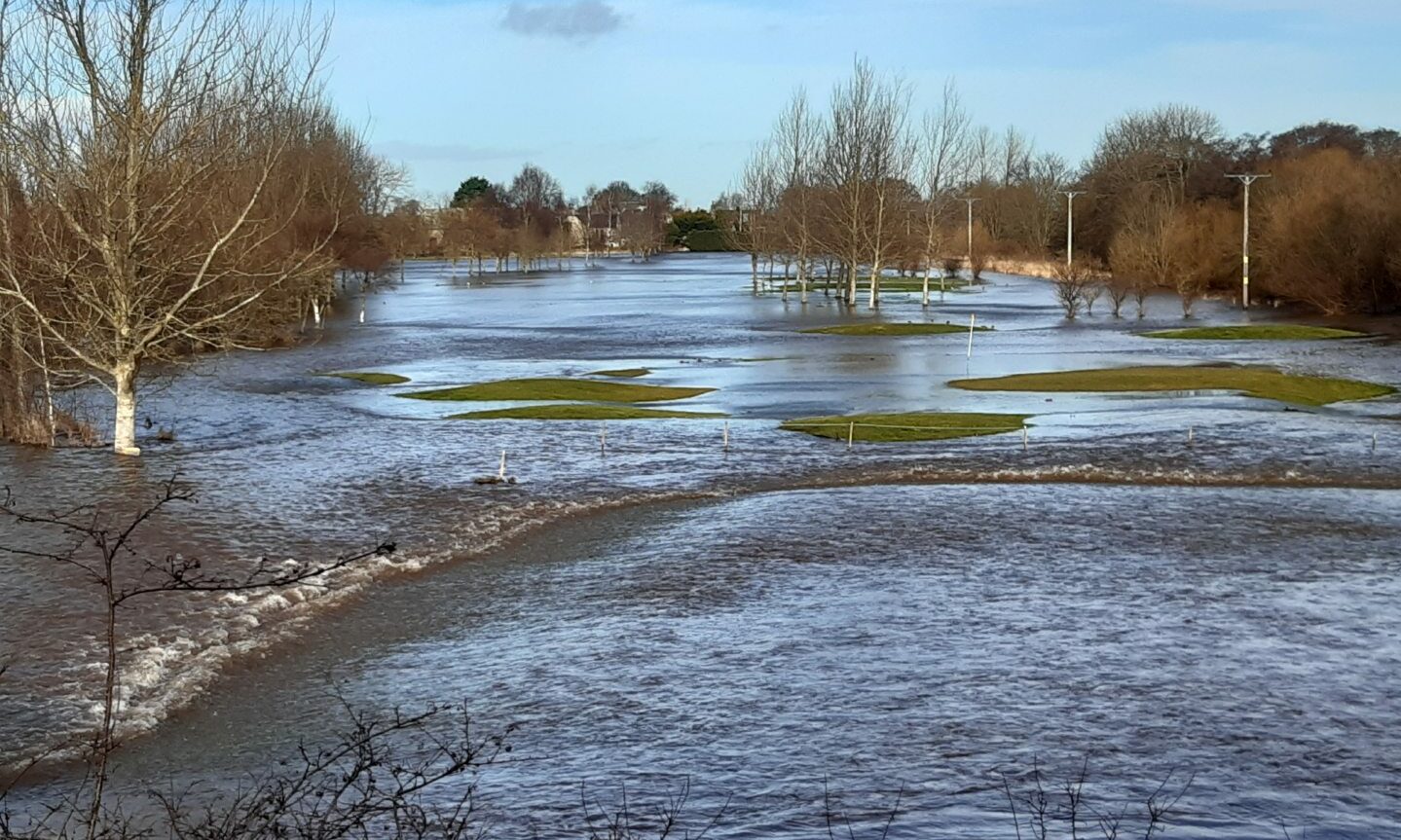 View of Garmouth Golf Club from railway viaduct with water rushing across course. 