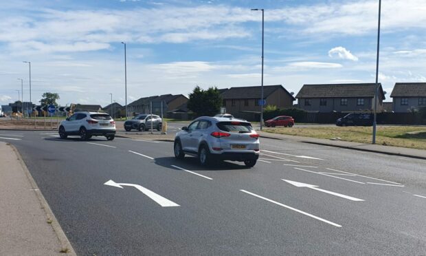Cars on A96 at KFC roundabout with arrows on the road, left in left lane, straight ahead in right lane.