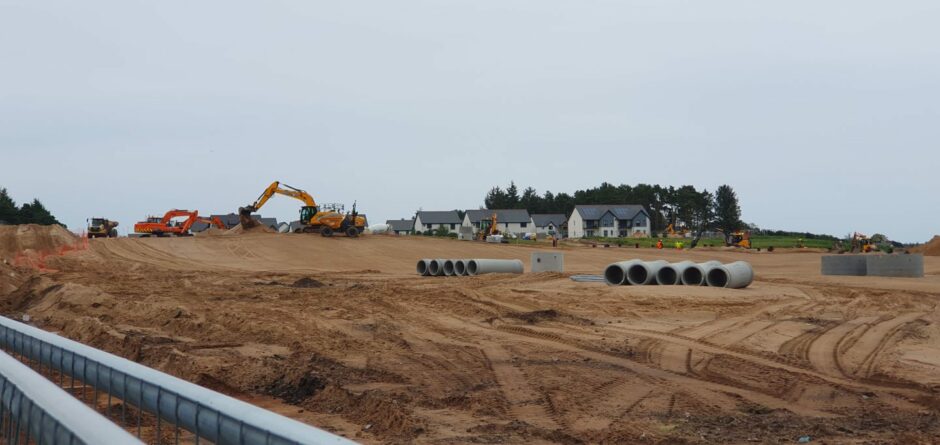 Construction vehicles on large sandy land with homes in background.