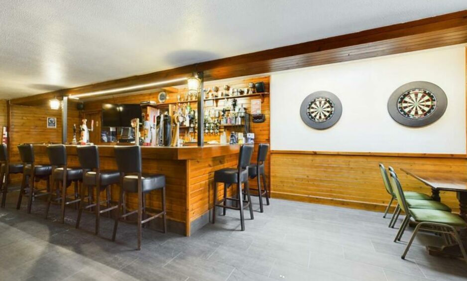 The bar in the hotel, with a rustic wooden bar, an abundance of bar stools and two dartboards