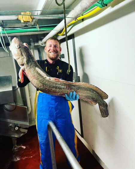 Connel Gresham standing up and holding a large fish.