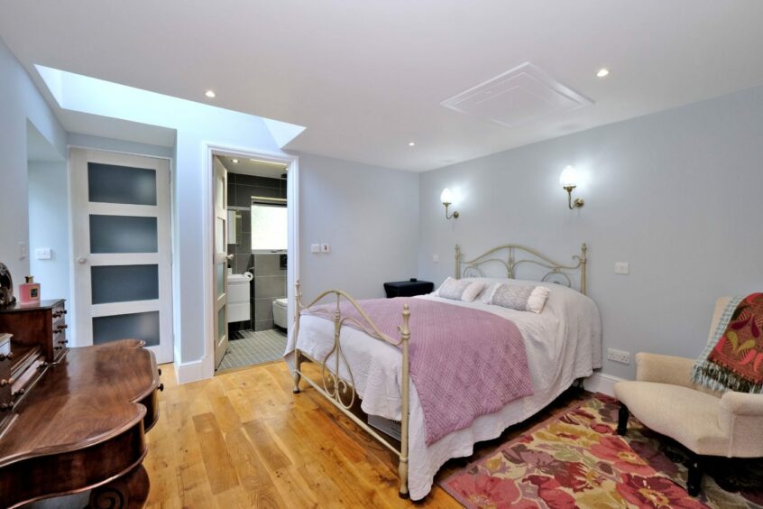 A bedroom in the property with an en suite bathroom. The room includes a dark wooden dresser, a metal-framed bed, a cream armchair and a floral rug.