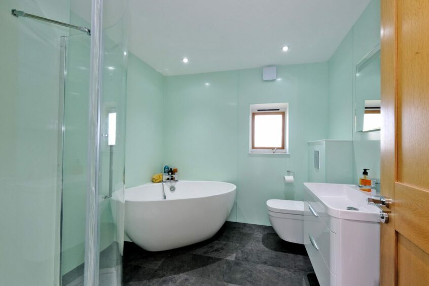 The bathroom in the Four-bedroom steading conversion in Aberdeenshire, with pale green walls, dark grey floor tiles, a corner-set shower, a freestanding bath with matching toilet and sink