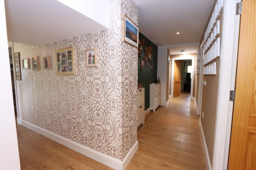 The hallway with a patterned wallpaper on one section of the wall and green and brown paint on the others