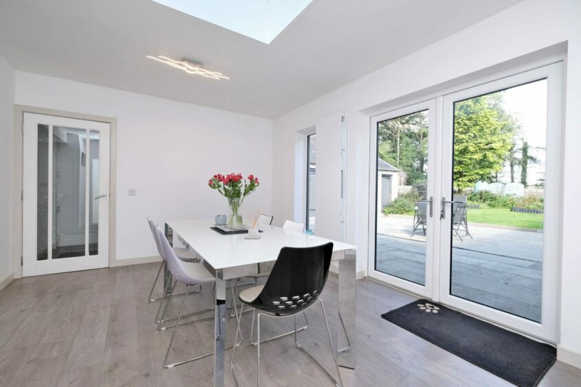 The dining room in the schoolhouse in Durno, with white walls, grey laminate flooring and  glass patio doors leading to the garden.