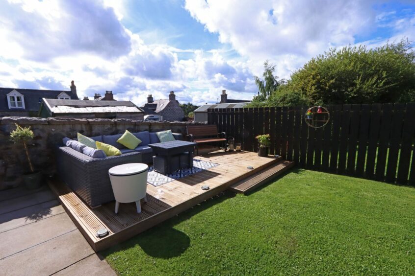 The garden of the cottage with a green lawn, wooden patio and grey patio furniture