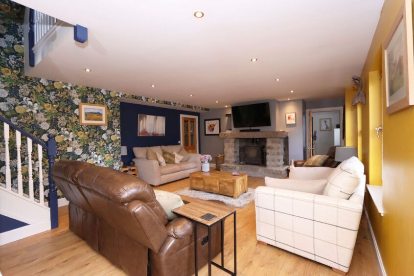 The living room of the cottage with three sofas, a wooden coffee table, a large fireplace and navy blue and yellow walls