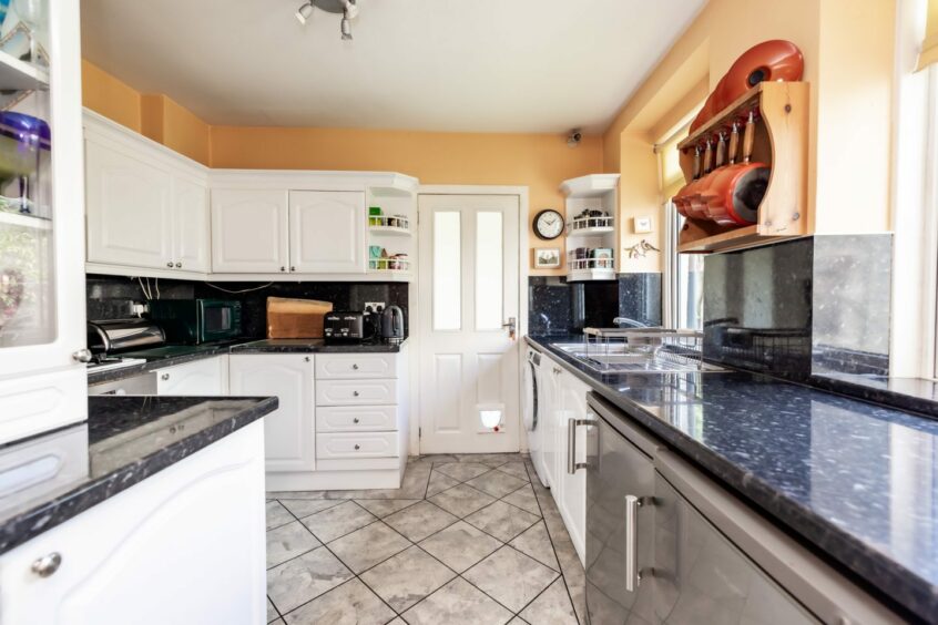 The kitchen in the home has cheery yellow walls, grey floor tiles, white counters and cupboards with black and white counters.