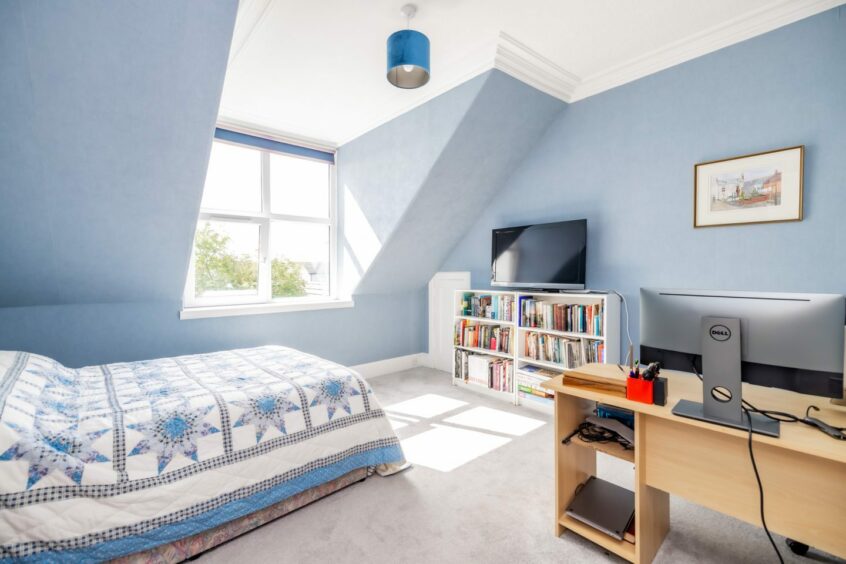 A bedroom in the period property in Aberdeen, with a double bed, a desk perfect from working from home and a bookcase with a flatscreen TV perched on top. The walls are a light shade of blue with a matching bedspread and lightshade on the ceiling.