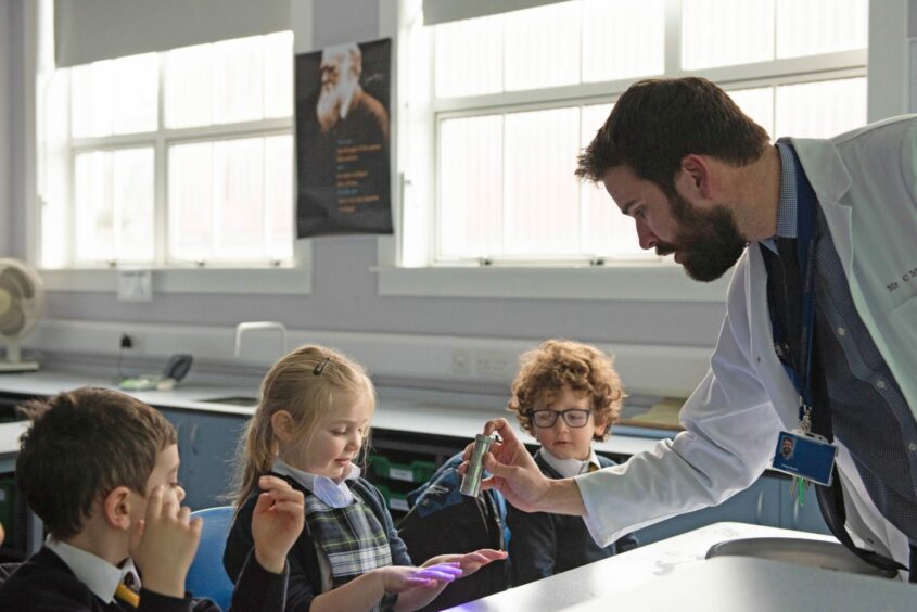 male teacher shows his three pupils in class how a torch works. this is part of the primary curriculum in Scotland's schools