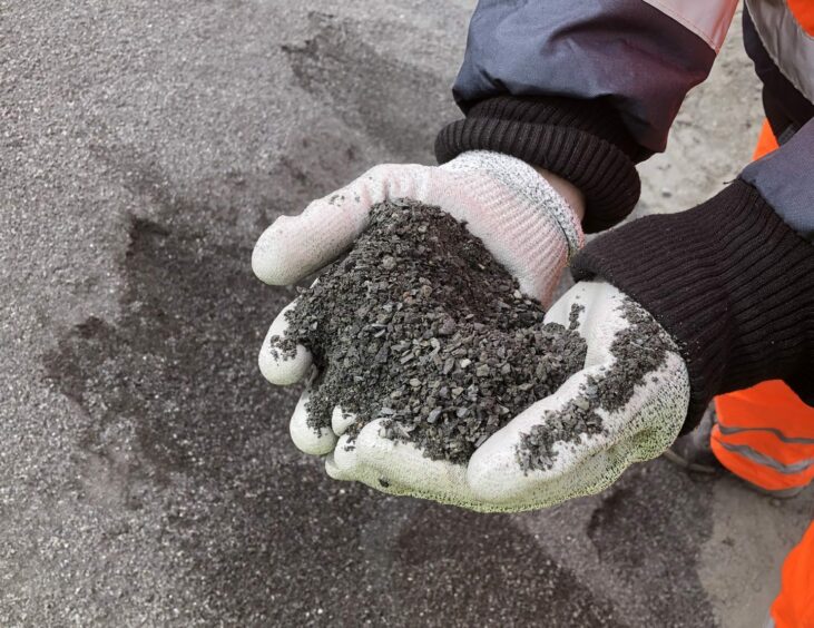 A person wearing white gloves holds a handful of basalt dust.