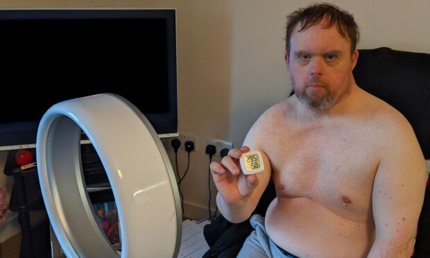 Gavin Henderson in his Inverurie care home sitting topless in front of a fan looking unhappy.