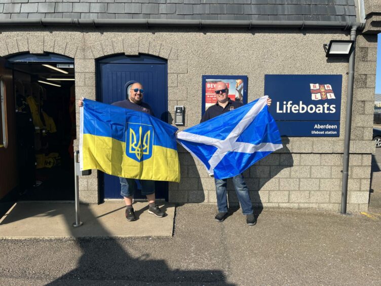 RNLI crew Cal Reed and Grant Bruce holding Ukraine and Scotland flags at Aberdeen Lifeboat Station.
