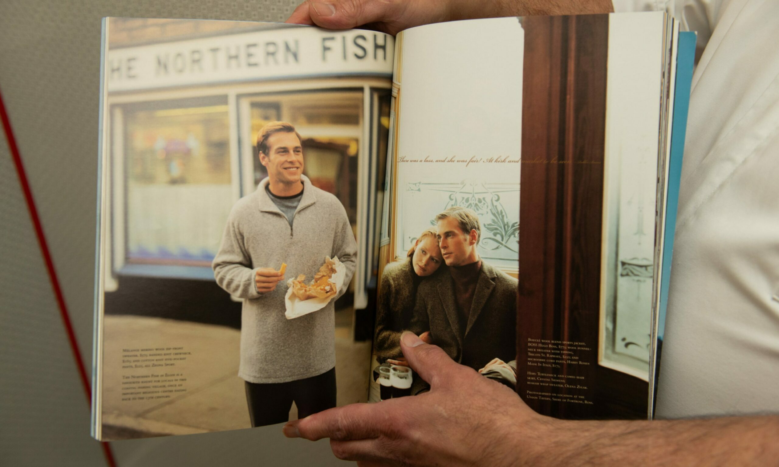 Michael Miele holding up a magazine showing a man eating chips smiling outside Northern Fish Restaurant. 