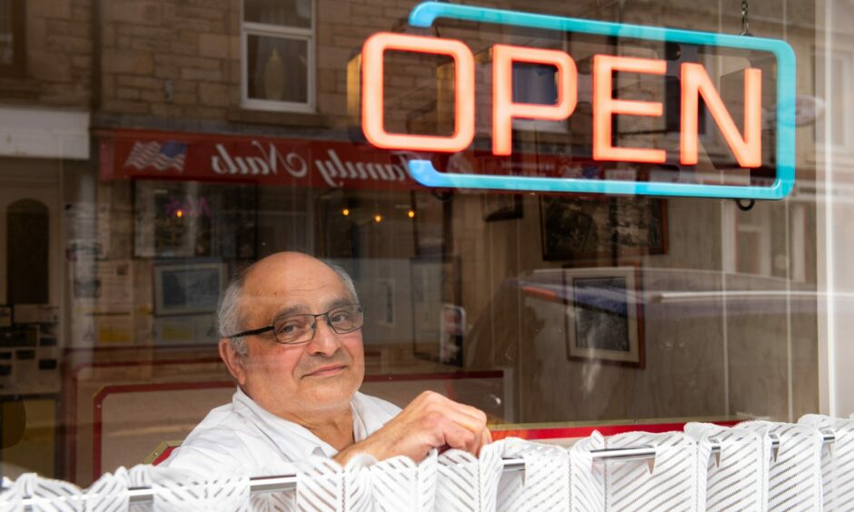 Michael Miele looking through the window of the Northern Fish Restaurant below an open sign.