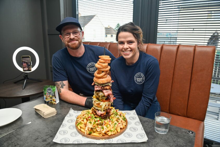 Mike and Jen McEwan in a booth with Elgin's Humble Burger challenge on the table in front of them