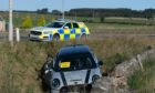 A Mini Cooper car in a ditch following a crash with a police car in the background