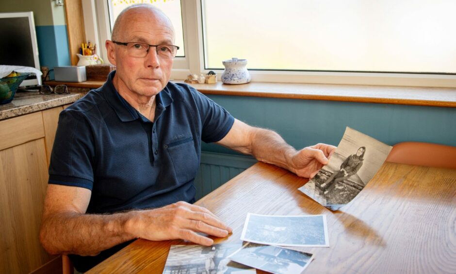 Robert McCready sitting at a table with photos of his sister Carole McLay laid out in front of him