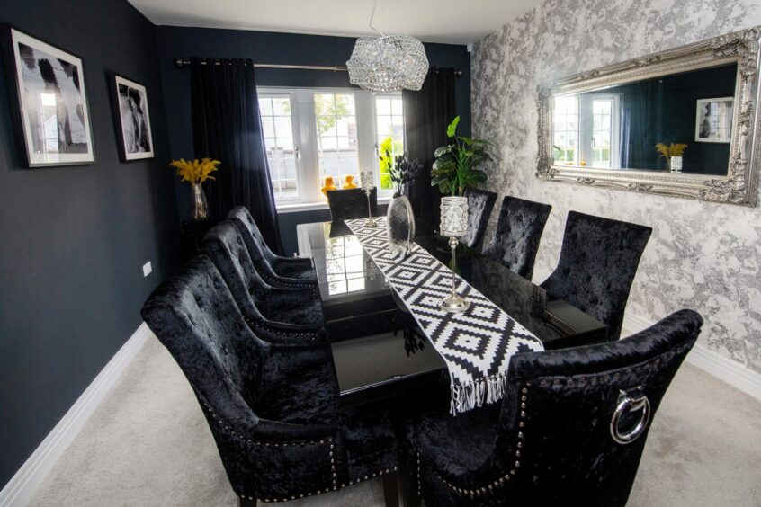 The dining room in the Cults interior designer's home. There is a black dining table with eight black chairs, black walls and a grey patterned feature wall