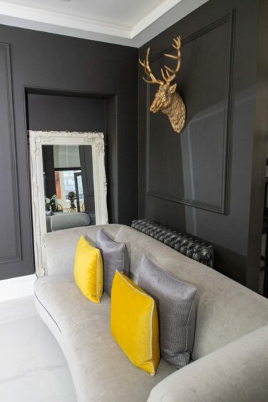 The sofa in the lounge with a white framed mirror next to it and a gold faux deer head hung over it