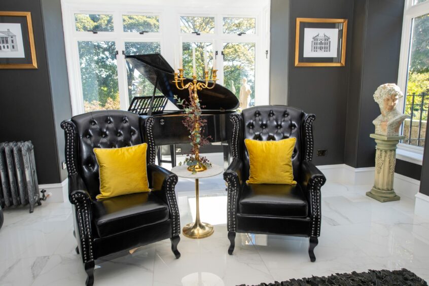 The two matching black armchairs with the grand piano behind it