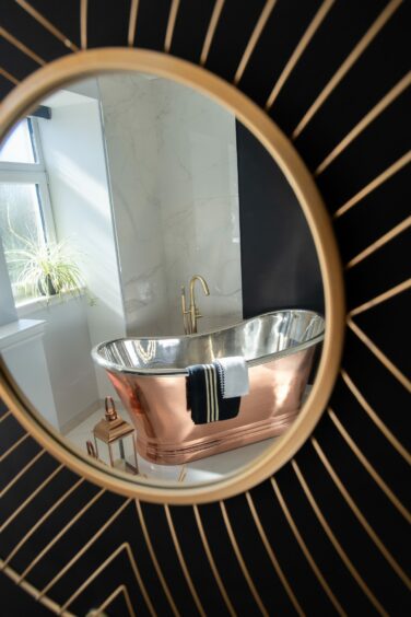 The freestanding copper bath reflected in the gold-framed statement mirror