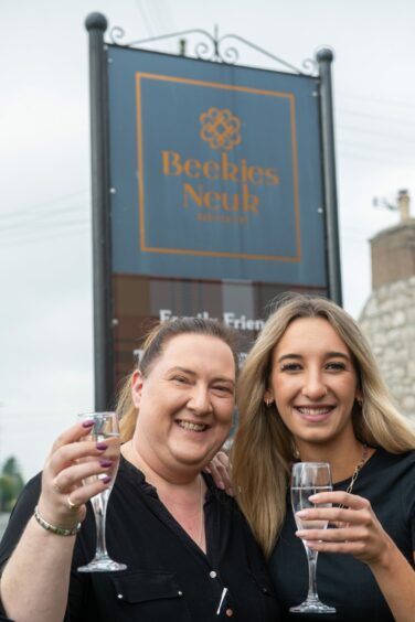 Emily Gill and Fiona Bisset pose with champagne outside the premises blue sign.