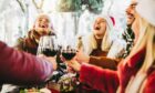 Group of people with wine and santa hats laughing.