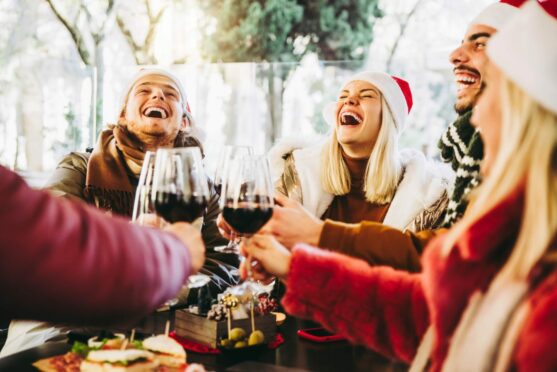 Group of people with wine and santa hats laughing.