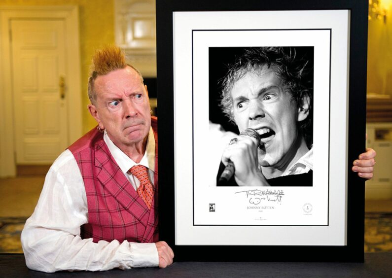 John Lydon with a signed archive photograph of him from his Sex Pistol days that reads: 'Johnny Rotten'.