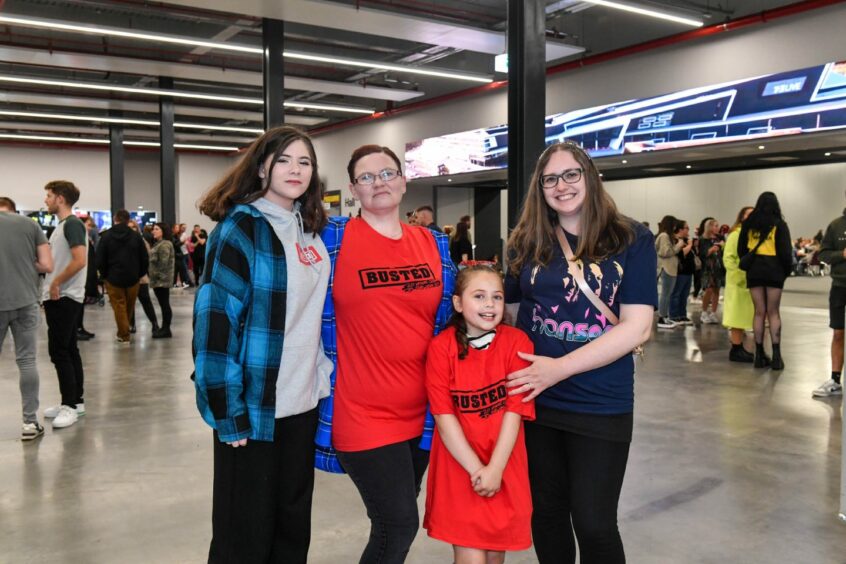 Three women of different ages and a little girl. The two women on the left are wearing busted t-shirts, the young girl is wearing a Busted T-shirt as a dress and the woman on the right is wearing a Hanson T-shirt