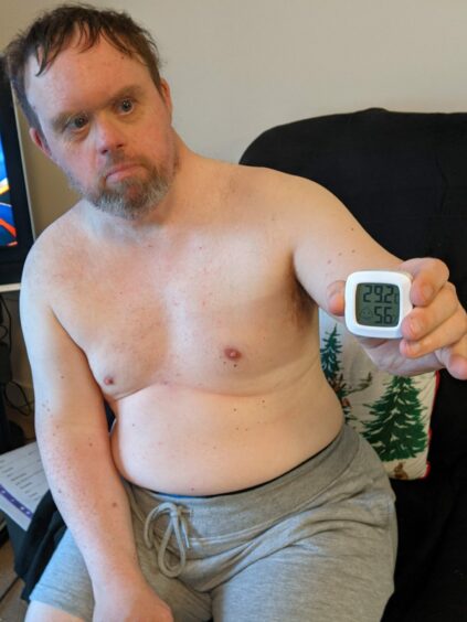 Gavin sitting topless in his living room at Inverurie care home St James Court with a thermometer showing 29.2C
