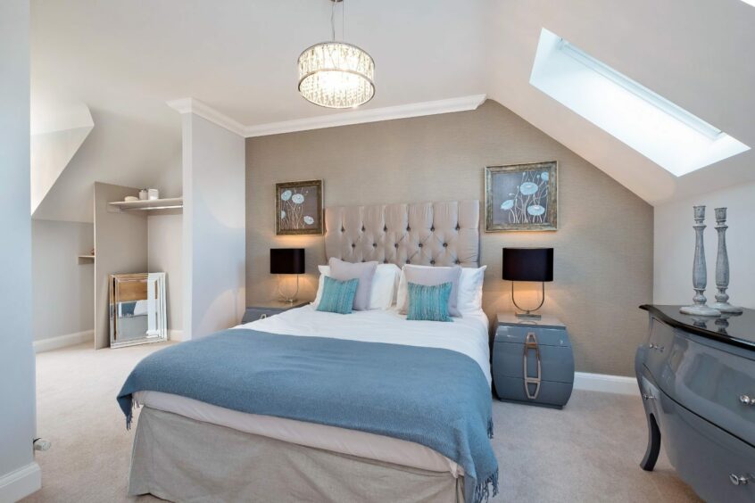 A bedroom with slanted ceilings, off-white walls and carpet and light blue accents