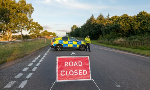 A police car sits in the middle of the A96 behind a road closed sign.