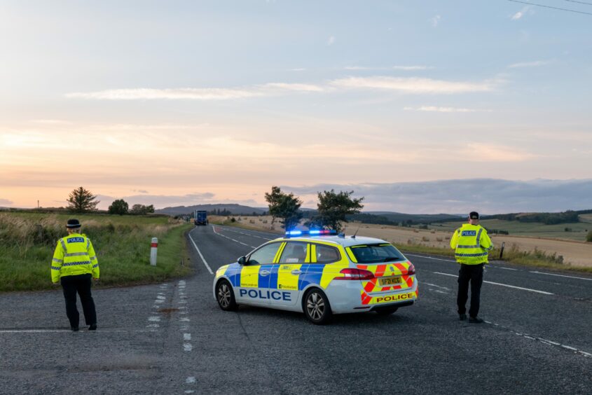 Police officers stand beside a police car as they monitor the A96.