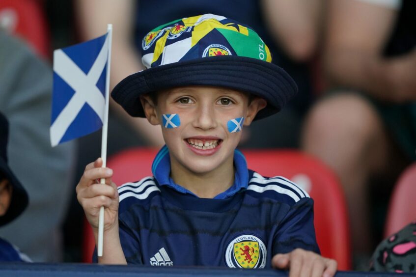 A young Scotland fan in the stands with the flag painted on his cheeks and a flag in his hand