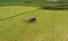 A tractor driving down the centre of a green field.
