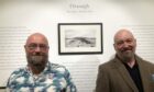Stephen Ely and Michael Faint stand smiling in front of an art gallery wall.